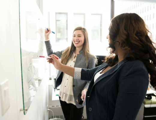 2 Women Standing in Front of a Whiteboard